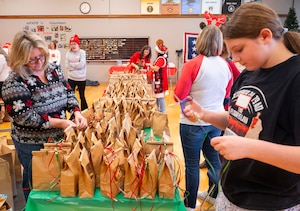 Women stand on either side of a long table working on bags of cookies.