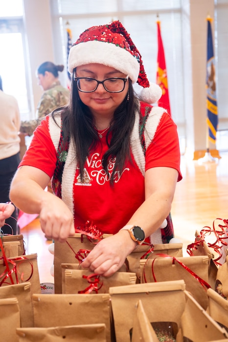 A woman wearing a Santa hat and a red shirt ties ribbons to paper bags.