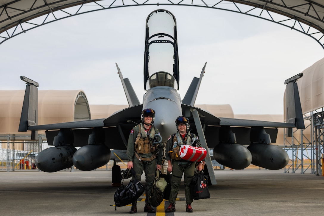 U.S. Navy Lt. Cmdr. Sean McCormick, top left, a naval aviator, and Lt. Tyler Sost, a weapons system officer, and a native of Egg Harbor Township, New Jersey, both with Strike Fighter Squadron (VFA) 102, Carrier Air Wing (CVW) 5, Carrier Strike Group 5, pose for a photo in front of a F-18F Super Hornet aircraft at Marine Corps Air Station Iwakuni, Japan, Dec. 10, 2025. CVW-5 aircraft and personnel returned to MCAS Iwakuni from the Nimitz-class aircraft carrier USS George Washington (CVN-73), where they provided air superiority, all-weather offensive air-to-surface attack capabilities. (U.S. Marine Corps photo by Cpl. Dahkareo Pritchett)