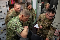 Four people in military uniforms gather around a launch control center.