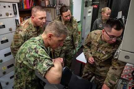 Four people in military uniforms gather around a launch control center.