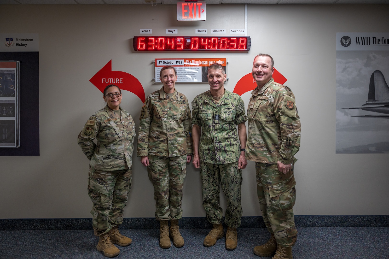 Four people in military uniforms pose in front of a clock.