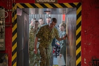 A man in a navy uniform walks through a blast door.