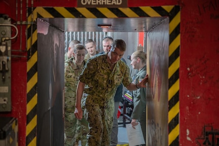 A man in a navy uniform walks through a blast door.