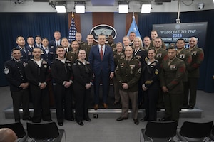 A large group of people in various dress military uniforms pose for a photograph with a man in the center of the group wearing civilian business attire.