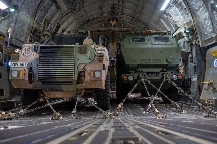 a shot of two military vehicles from the front taken in a military cargo plane with chains holding each vehicle in place