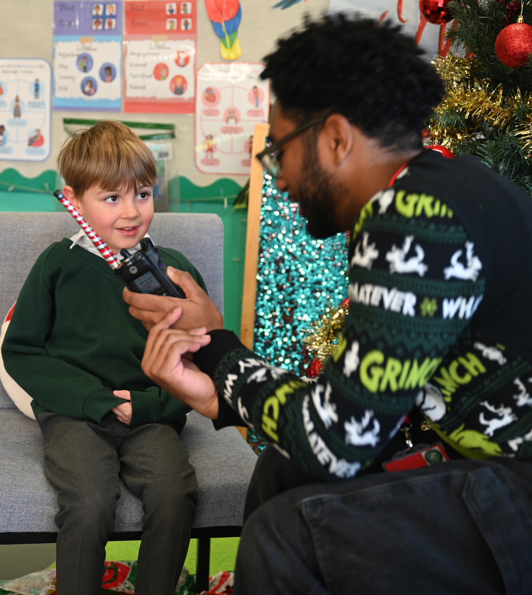 U.S. Air Force Airman 1st Class Jeffrey Favor, right, 100th Communications Squadron radiofrequency transmissions technician, RAF Mildenhall, uses a handheld radio to help a Year-1 child interact with Santa at Great Heath Academy in Mildenhall, Suffolk, Dec. 10, 2025. Three Team Mildenhall members spent time with 47 children and provided them a chance to talk to Santa and make special gift requests before the holidays (U.S. Air Force photo by Karen Abeyasekere)