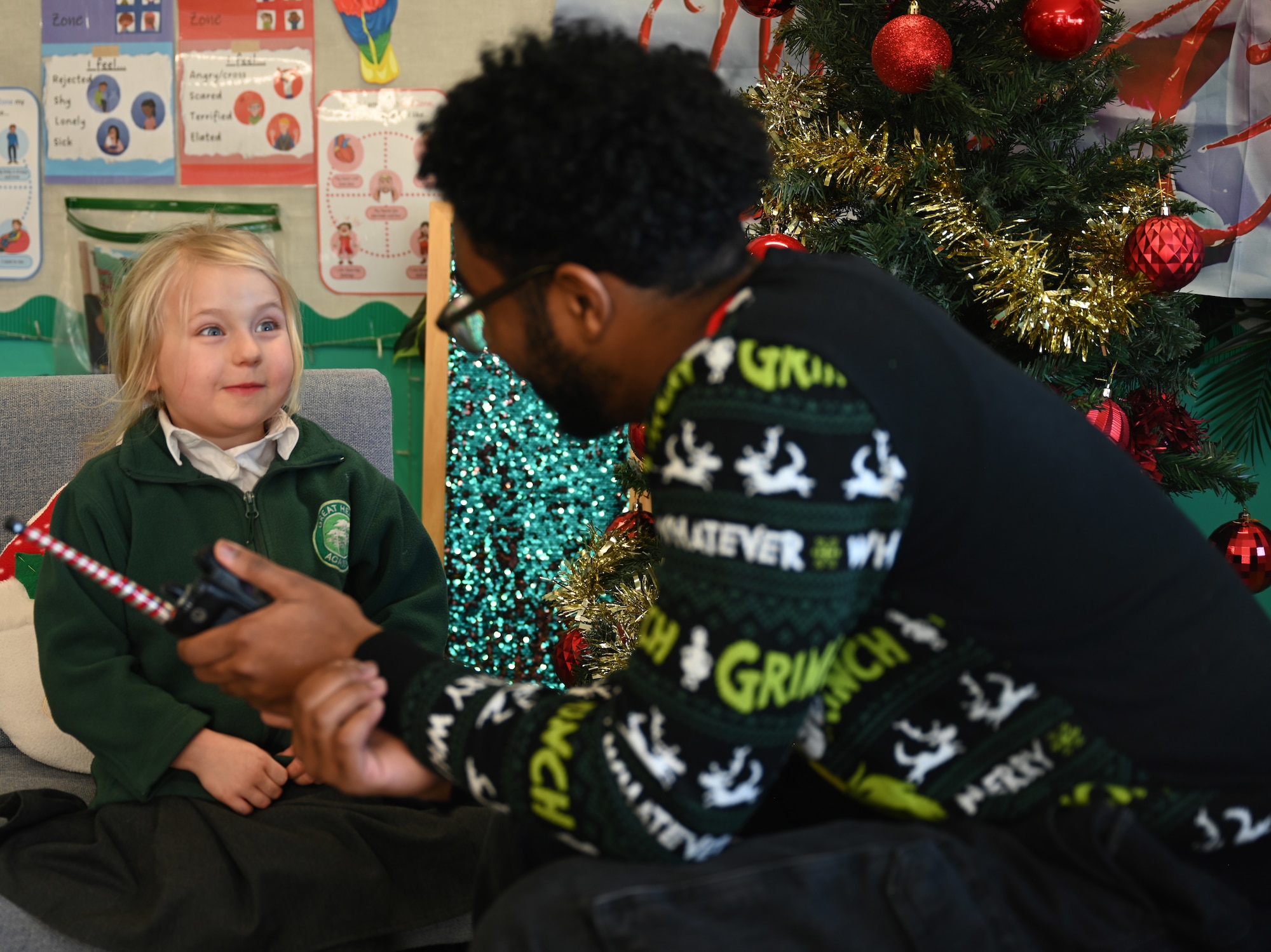 U.S. Air Force Airman 1st Class Jeffrey Favor, right, 100th Communications Squadron radiofrequency transmissions technician, uses a handheld radio to help a Year-1 child interact with Santa at Great Heath Academy in Mildenhall, Suffolk, Dec. 10, 2025. Three Team Mildenhall members spent time with 47 children and provided them a chance to talk to Santa and make special gift requests before the holidays. (U.S. Air Force photo by Karen Abeyasekere)
