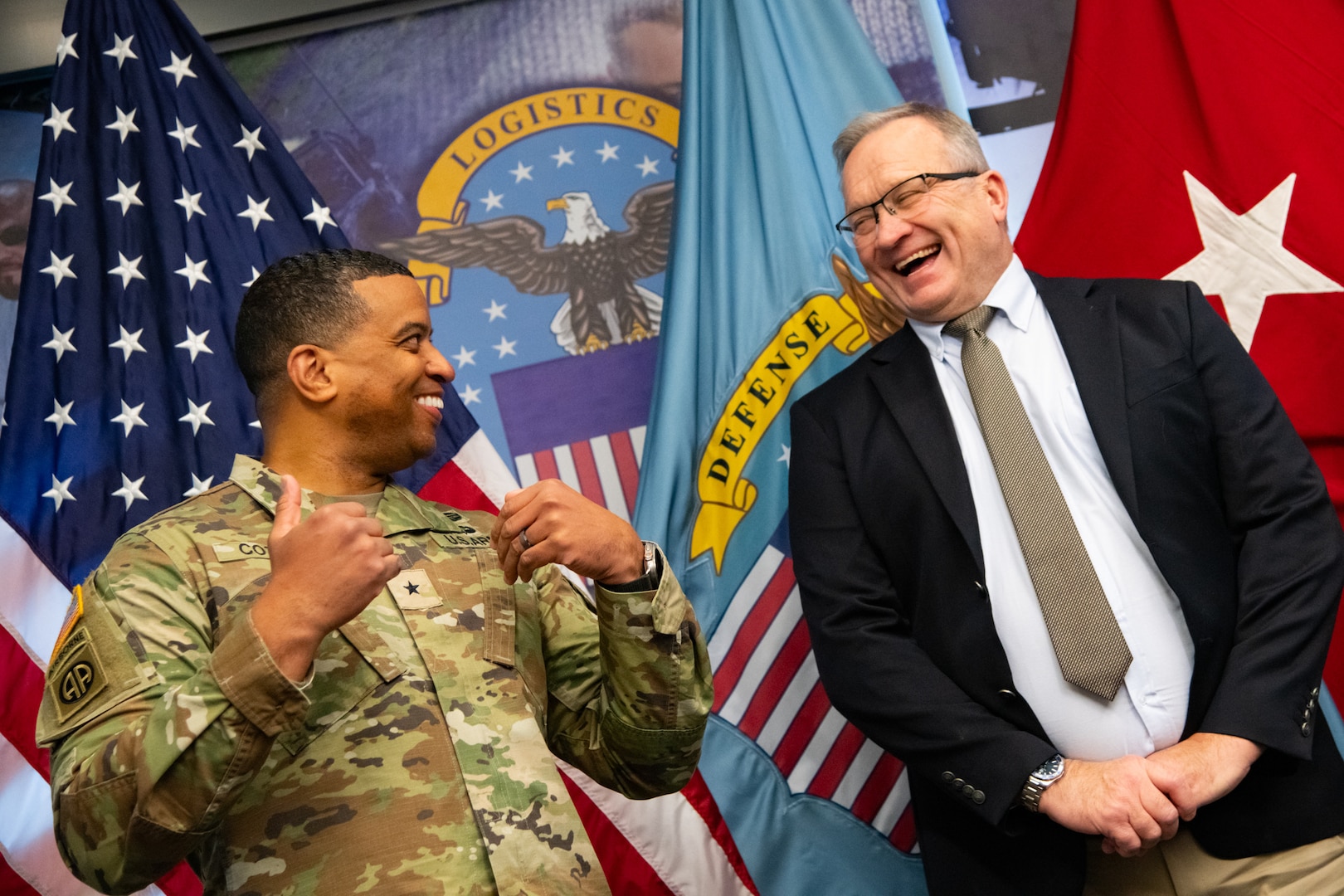 Two people at an award ceremony standing in front of flags.