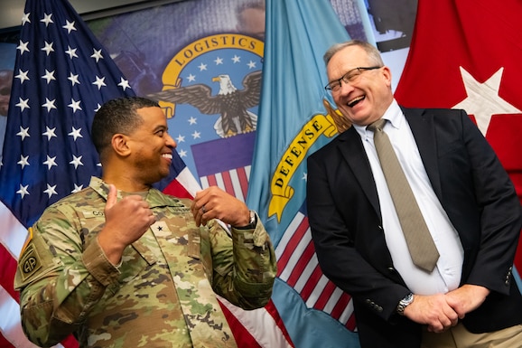 Two people at an award ceremony standing in front of flags.