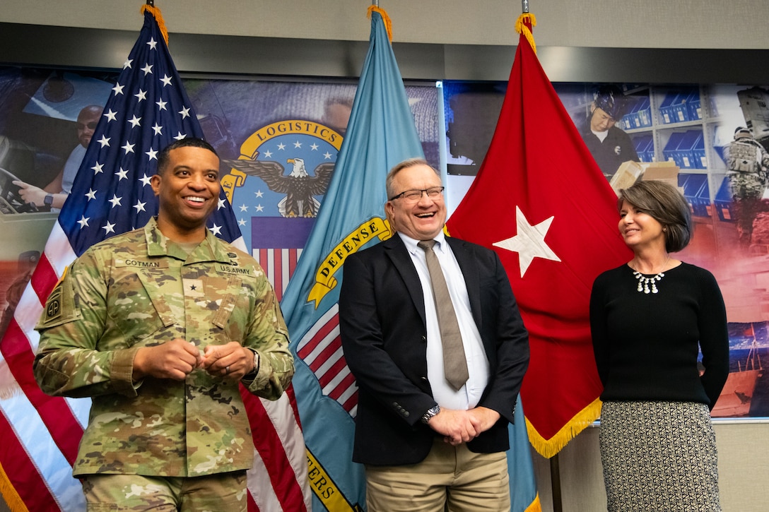 Two people at an award ceremony standing in front of flags.