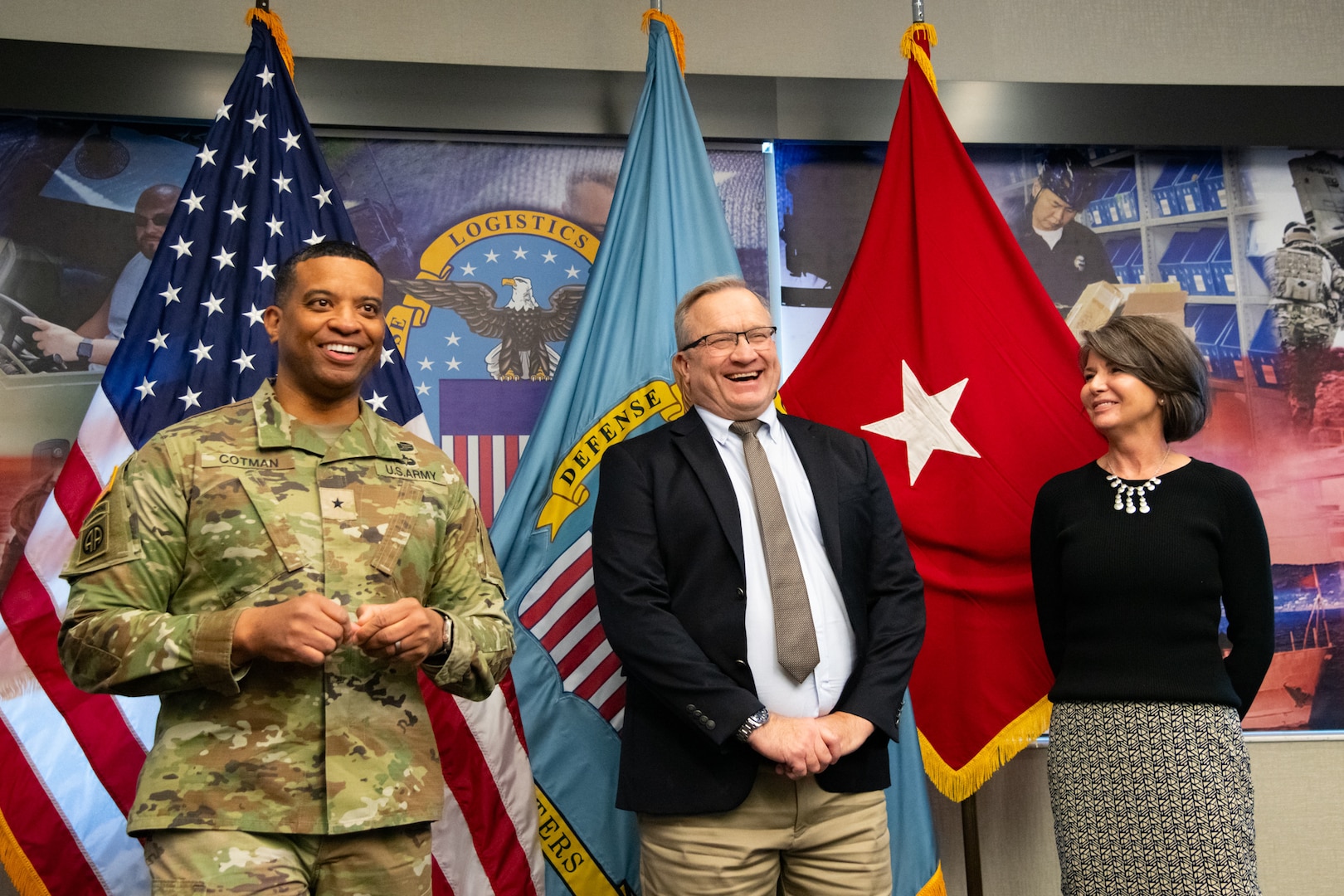 Two people at an award ceremony standing in front of flags.
