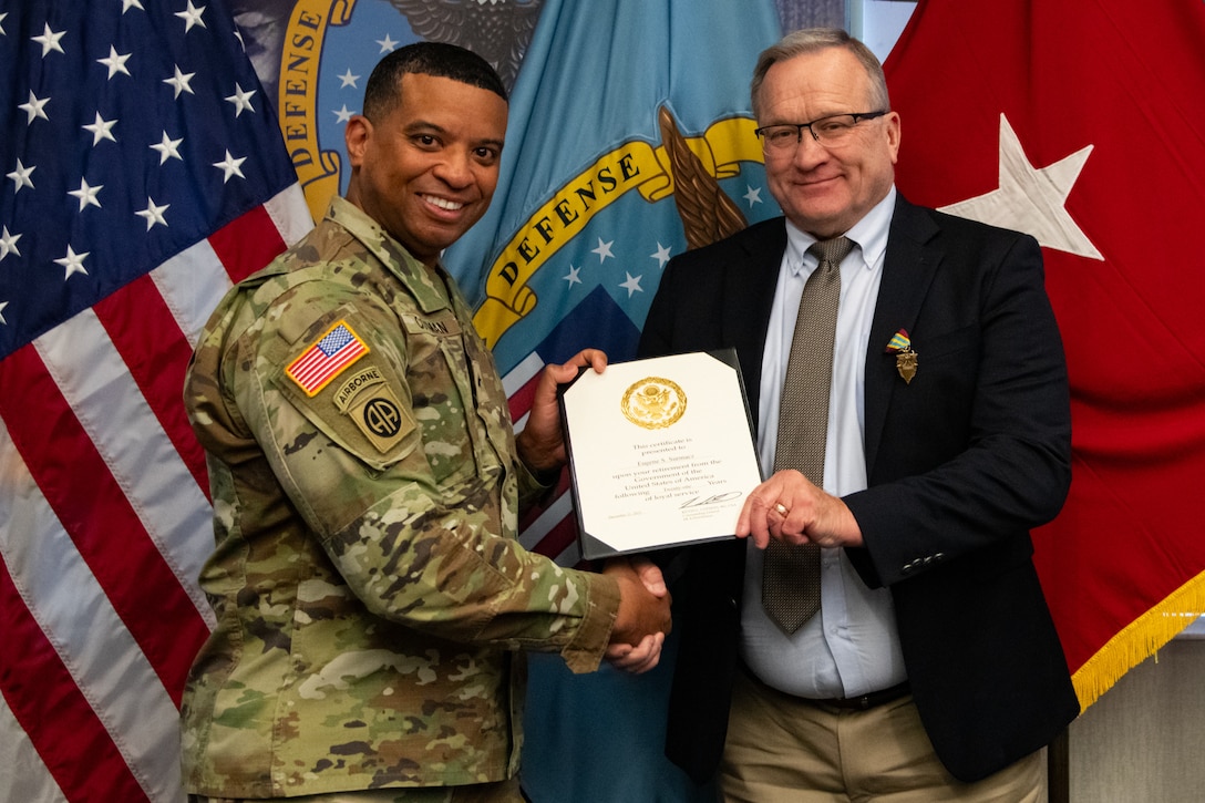 Two people at an award ceremony standing in front of flags.
