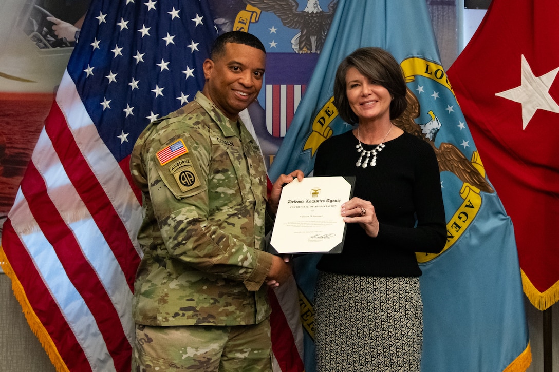 Two people at an award ceremony standing in front of flags.