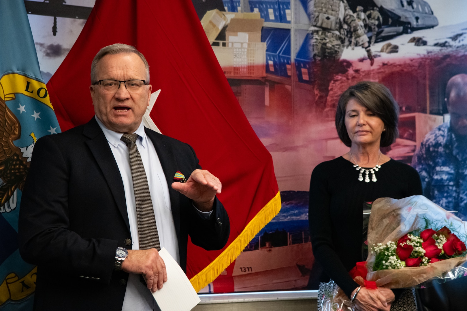 Two people at an award ceremony standing in front of flags.