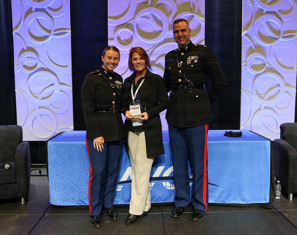 U.S. Marine Corps Capt. Riley Tejcek, an officer procurement officer with the Western Recruiting Region, left, U.S. Marine Corps Maj. Philip, current operations officer with Headquarters Company, 2nd Marine Regiment, 2nd Marine Division, right, and Shel Delisle, Head women’s volleyball coach at Milwaukee Area Technical College, present the award at the 2025 American Volleyball Coaches Association Convention – Battles Won Award during the AVCA Honors Luncheon in Kansas City, Missouri, Dec. 18, 2025. Delisle was awarded the Battles Won Award for her resilience and determination in overcoming a career-altering spinal injury through multiple surgeries and intensive rehabilitation. The Marine Corps hosted the awards luncheon during the AVCA Convention. (U.S. Marine Corps photo by Cpl. Hana Lathrop)