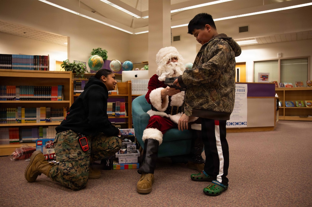 U.S. Marine Corps Capt. Daniel Kelly, dressed as Santa Claus, and Lance Cpl. Ariel Dutt, hand out gifts to children attending Fred Ipalook Elementary School in Utqiagvik, Alaska, Dec. 11, 2025. Dutt, an administrative clerk as well as Texas native, and Kelly, a military police officer and Inspector Instructor with 4th Law Enforcement Battalion, Force Headquarters Group, delivered toys to the school with the assistance of Marines from Detachment Delta Company and U.S. Airmen from various units during this year’s Toys for Tots operation. The Toys for Tots mission exemplifies the Marine Corps spirit in the Last Frontier, strengthening community ties while sharpening the Marines' readiness for Arctic operations. (U.S. Marine Corps photo by Cpl. Orion Stpierre)