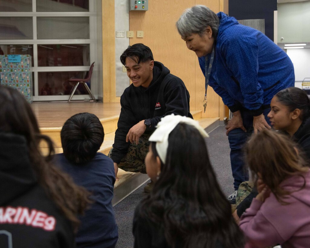 U.S. Marine Corps Gunnery Sgt. Niko Q. Azucenas greets a small class of children attending June Nelson Elementary School in Kotzebue, Alaska, Dec. 8, 2025. Azucenas is a military police officer with Detachment D Company, 4th Law Enforcement Battalion, Force Headquarters Group and is a native of Texas. Marines with 4th LEB delivered toys to the school with the assistance of U.S. Airmen from various units during this year’s Toys for Tots operation. The Toys for Tots mission exemplifies the Marine Corps spirit in the Last Frontier, strengthening community ties while sharpening the Marines' readiness for Arctic operations. (U.S. Marine Corps photo by Cpl. Orion Stpierre)