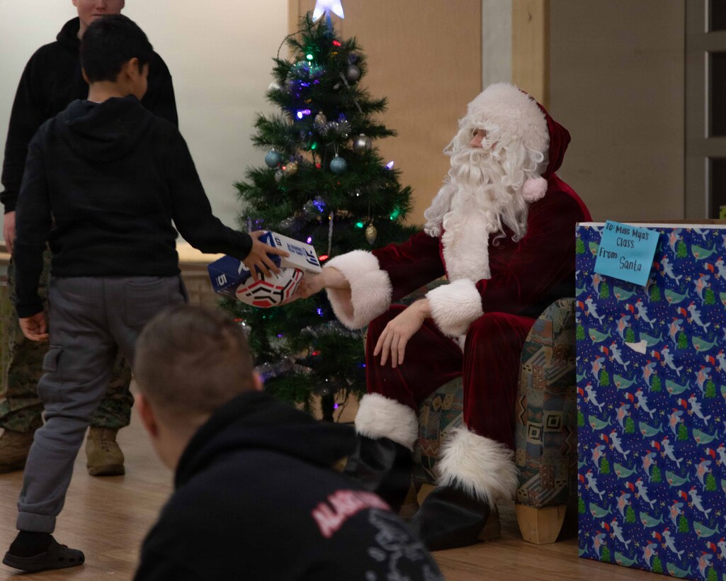 U.S. Marine Corps Capt. Daniel Kelly dressed as Santa Claus, greets a child attending June Nelson Elementary School in Kotzebue, Alaska, Dec. 8, 2025. Kelly, a military police officer and Inspector Instructor with 4th Law Enforcement Battalion, Force Headquarters Group delivered toys to the school with the assistance of Marines from Detachment Delta Company and U.S. Airmen from various units during this year’s Toys for Tots operation. The Toys for Tots mission exemplifies the Marine Corps spirit in the Last Frontier, strengthening community ties while sharpening the Marines' readiness for Arctic operations. (U.S. Marine Corps photo by Cpl. Orion Stpierre)