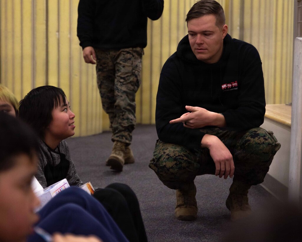 U.S. Navy Hospital Corpsman 2nd Class Curtis Darrow greets a child attending June Nelson Elementary School in Kotzebue, Alaska, Dec. 8, 2025. Darrow is a Colorado native with Detachment D Company, 4th Law Enforcement Battalion, Force Headquarters Group. The Marines with 4th LEB delivered toys to the school with the assistance of U.S. Airmen from various units during this year’s Toys for Tots operation. The Toys for Tots mission exemplifies the Marine Corps spirit in the Last Frontier, strengthening community ties while sharpening the Marines' readiness for Arctic operations. (U.S. Marine Corps photo by Cpl. Orion Stpierre)