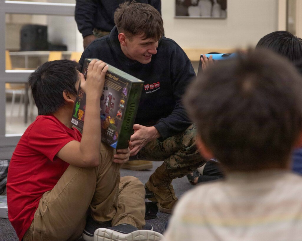 U.S. Marine Corps Lance Cpl. Owen Long greets two children who received presents at June Nelson Elementary School in Kotzebue, Alaska, Dec. 8, 2025. Long is a native of Waynesboro, Pennsylvania and a combat videographer with Communications Strategy and Operations, Marine Forces Reserve. The Marines assigned to Detachment D Company, 4th Law Enforcement Battalion, Force Headquarters Group and the airmen assigned to the 673rd Security Forces Squadron are participating in Operation Polar Knight in support of the Toys for Tots mission reaching remote Alaskan communities.