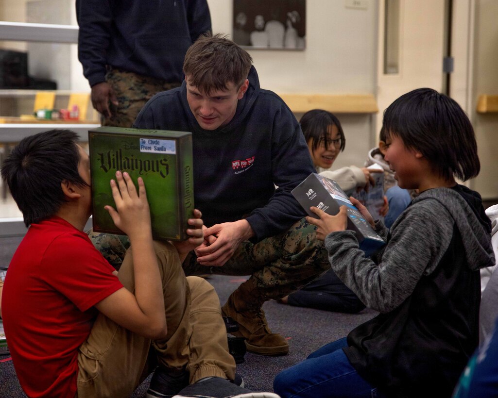 U.S. Marine Corps Lance Cpl. Owen Long greets two children who received presents at June Nelson Elementary School in Kotzebue, Alaska, Dec. 8, 2025. Long is a native of Waynesboro, Pennsylvania and a combat videographer with Communications Strategy and Operations, Marine Forces Reserve. The Marines assigned to Detachment D Company, 4th Law Enforcement Battalion, Force Headquarters Group and the airmen assigned to the 673rd Security Forces Squadron are participating in Operation Polar Knight in support of the Toys for Tots mission reaching remote Alaskan communities.