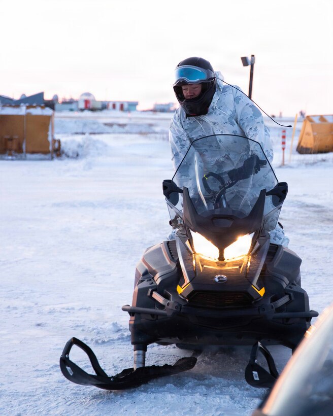 U.S. Marine Corps Sgt. Nicholas Baumbach, parks his snow machine while Marines off load the KC-130 in Kotzebue, Alaska, Dec. 04, 2025. Baumbach is an armorer and California native with Detachment Delta Company, 4th Law Enforcement Battalion, Force Headquarters Group. The Toys for Tots program highlights the Marine Corps' commitment to community support in the Arctic, while also enhancing the Marines’ preparedness for cold-weather operations. (U.S. Marine Corps photo by Cpl. Orion Stpierre)
