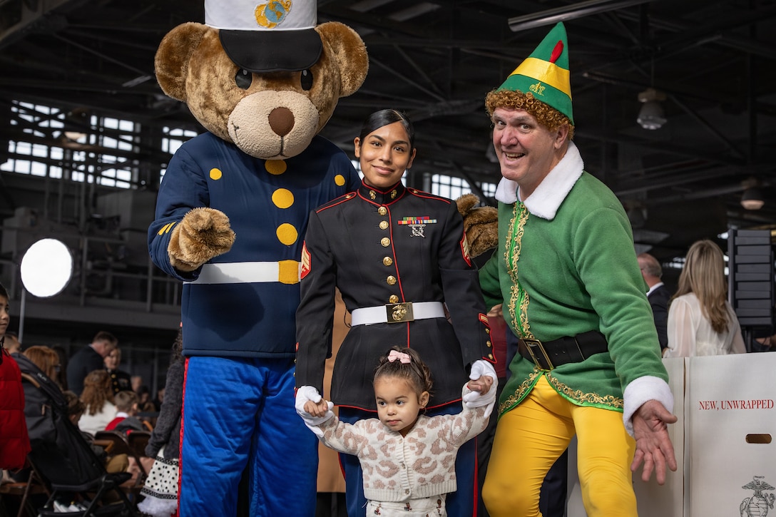U.S. Marine Corps Sgt. Casandra Curry, center, an administrative clerk with Navy and Marine Corps Appellate Leave Activity, Headquarters Marine Corps, and her daughter pose for a photo with Gunny Bear, left and Buddy the elf during a Toys for Tots charity event on Marine Corps Base Quantico, Virginia, Dec. 8, 2025. Since 1947, the Marine Corps Reserve has spearheaded the Toys for Tots program nationwide to collect toys for less fortunate children during the holiday season. Presently, the program distributes 7 to 18 million toys to children annually. (U.S. Marine Corps photo by Lance Cpl. Van Hoang)