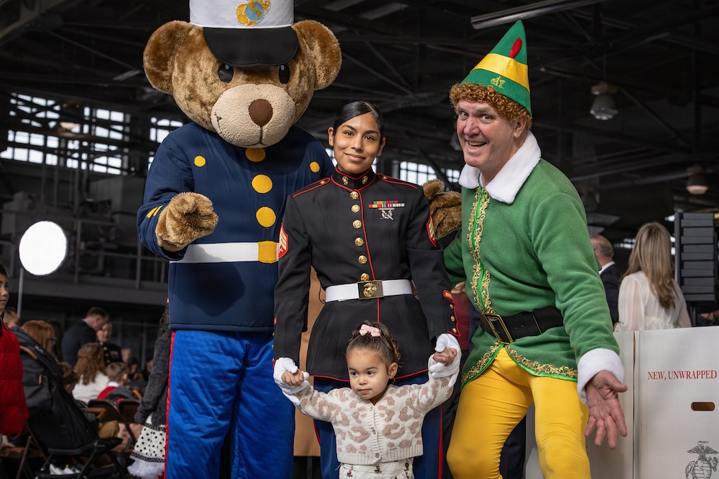 U.S. Marine Corps Sgt. Casandra Curry, center, an administrative clerk with Navy and Marine Corps Appellate Leave Activity, Headquarters Marine Corps, and her daughter pose for a photo with Gunny Bear, left and Buddy the elf during a Toys for Tots charity event on Marine Corps Base Quantico, Virginia, Dec. 8, 2025. Since 1947, the Marine Corps Reserve has spearheaded the Toys for Tots program nationwide to collect toys for less fortunate children during the holiday season. Presently, the program distributes 7 to 18 million toys to children annually. (U.S. Marine Corps photo by Lance Cpl. Van Hoang)