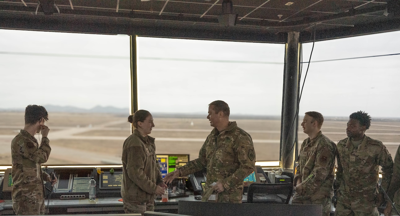 U.S. Air Force Col. Richard Kind, 97th Air Mobility Wing commander, coins U.S. Air Force Senior Airman Sarah Luce, 97th Operations Support Squadron air traffic control trainer, at Altus Air Force Base, Oklahoma, Dec. 15, 2025. Luce was recognized as the 2025 fiscal year Air Education and Training Command Airfield Operations Trainer of the Year, rewarding her exceptional performance and commitment to her duties. (U.S. Air Force photo by Airman 1st Class Emma Wright) 
This photo was altered for security purposes by blurring out flight monitors.