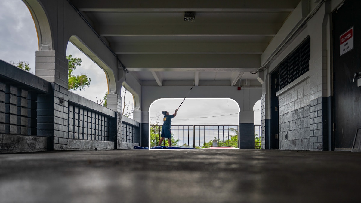 A sailor uses a cleaning tool to clean the exterior building arch of a middle school.