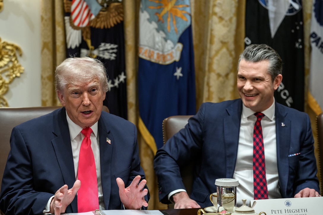 President Donald J. Trump speaks at a table as Secretary of War Pete Hegseth laughs.