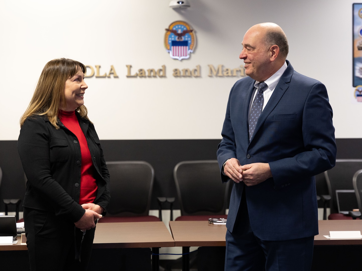 A man and a woman in business dress smile at each other.