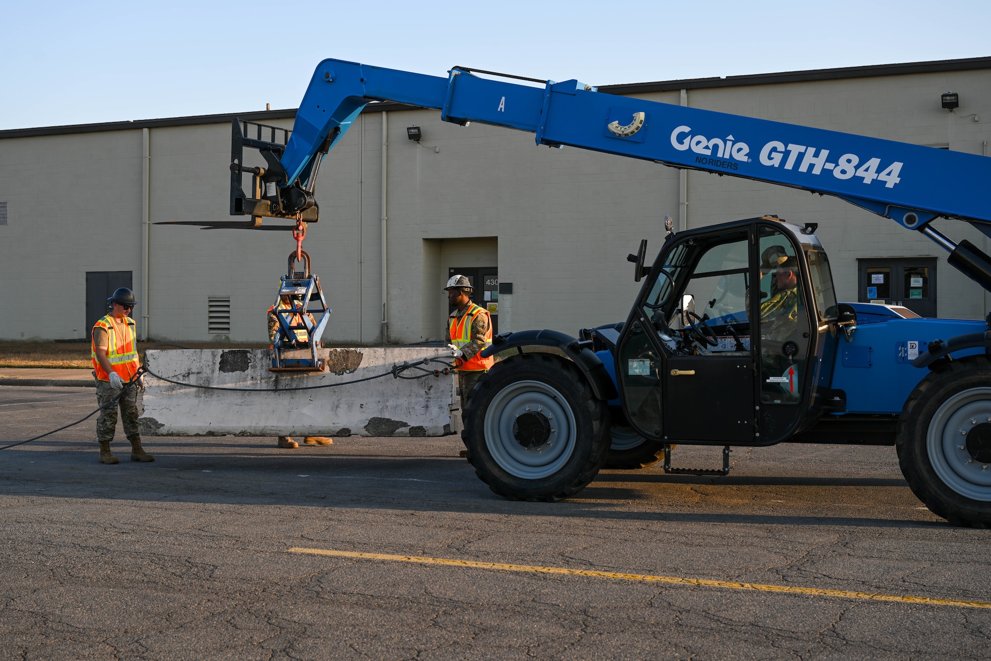 Airmen move a barricade into place in front of a building.