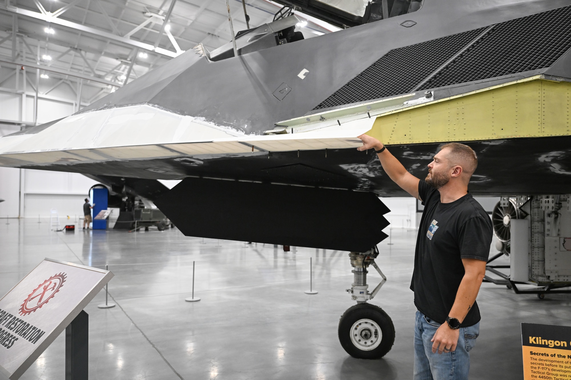 A man stands next to an aircraft in a museum pointing at a 3D printed part
