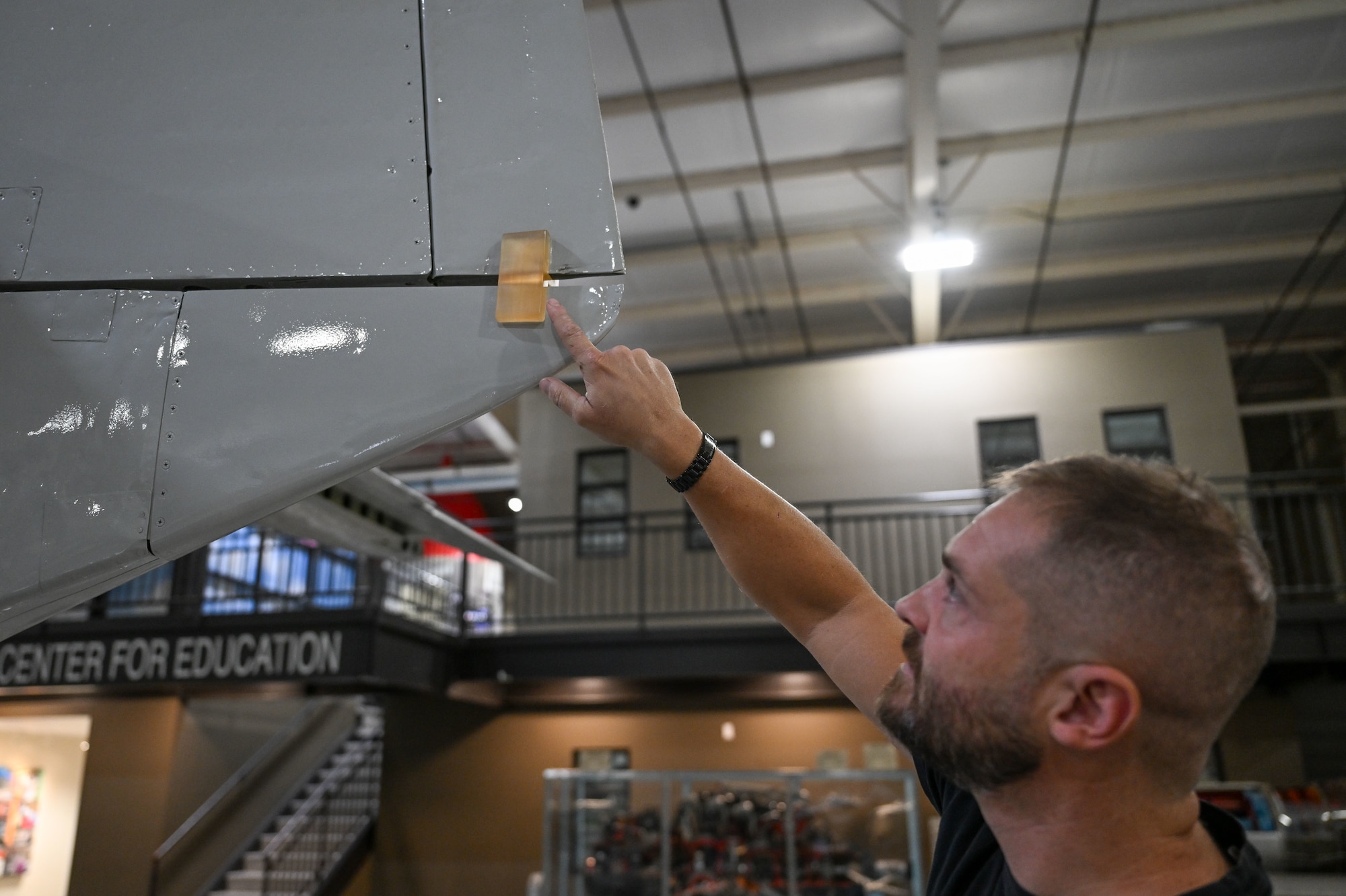 A man standing behind an aircraft pointing at a 3D part