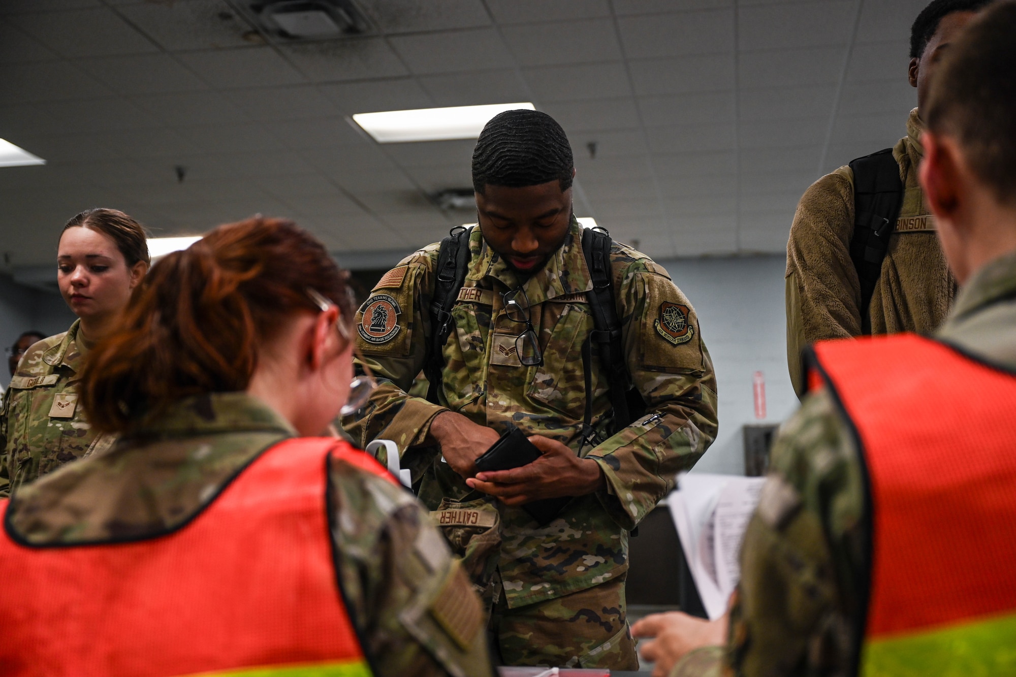 Air Force members process a simulated deployment line while members in orange vests check them in.