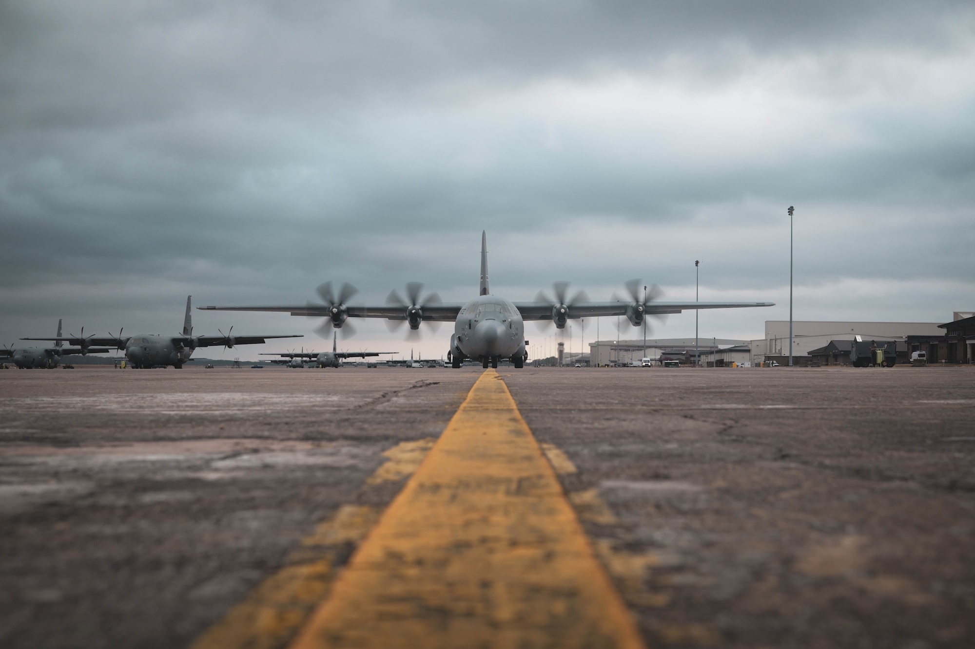 A C-130J Super Hercules aircraft sits on the flight line with its propellers in motion.
