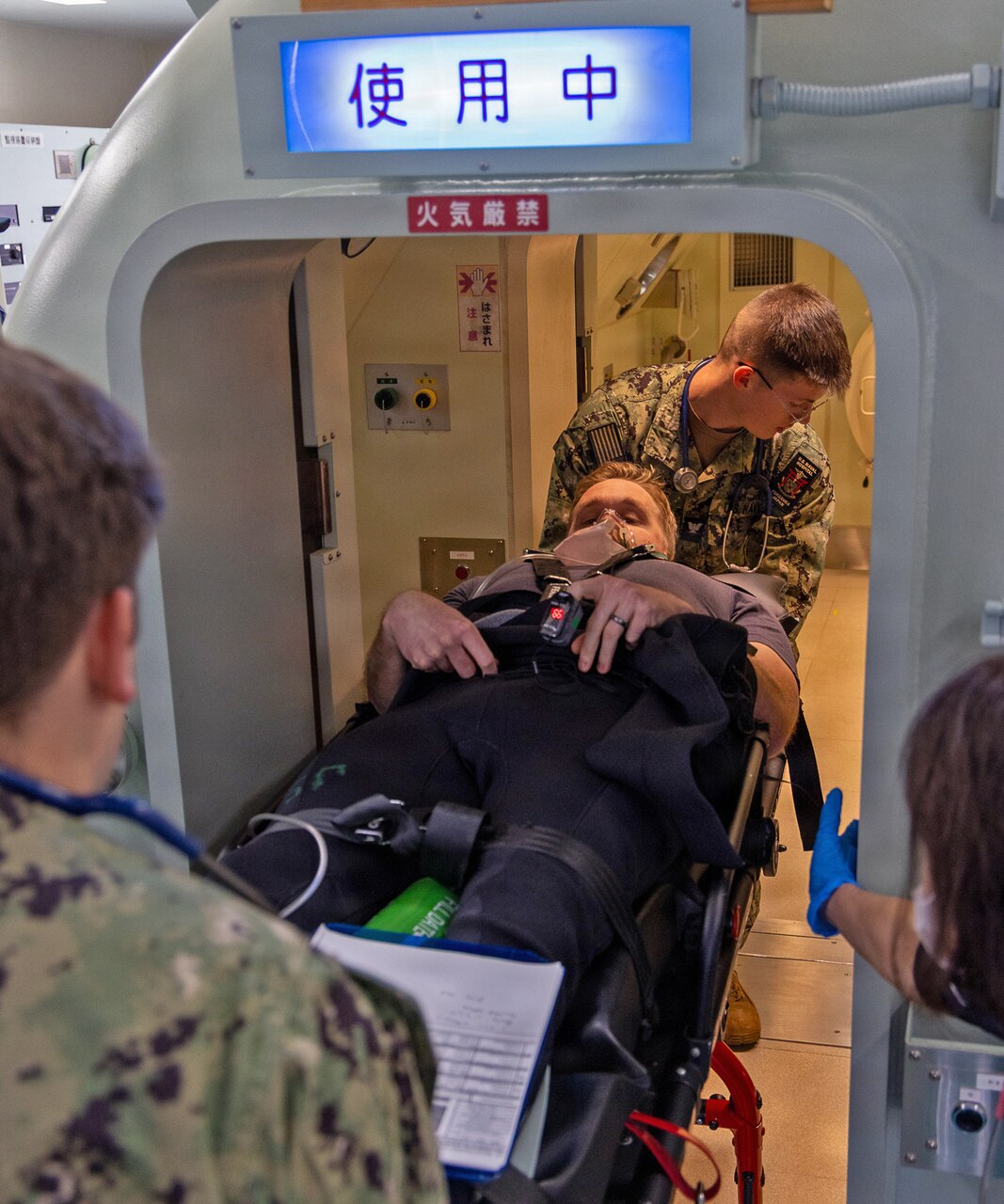 TAURA, Japan (Nov. 18, 2025) — U.S. Navy hospital corpsmen from U.S. Naval Hospital Yokosuka and Japan Maritime Self-Defense Force hyperbaric technicians prepare to move a simulated diving casualty into a hyperbaric chamber at the JMSDF Undersea Medical Center during a bilateral emergency response drill. The exercise rehearsed coordinated response, transport, and evaluation procedures for a simulated diving-related embolism. (U.S. Navy photo by Daniel Taylor/USNMRTC Yokosuka Public Affairs)