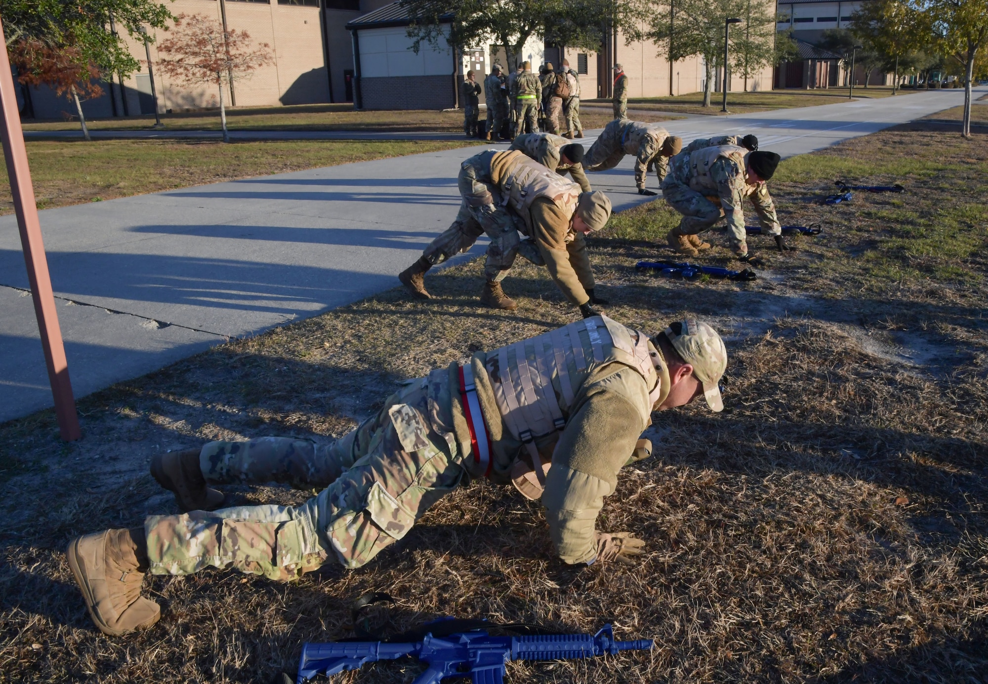 A group of people wearing military uniform perform burbees.