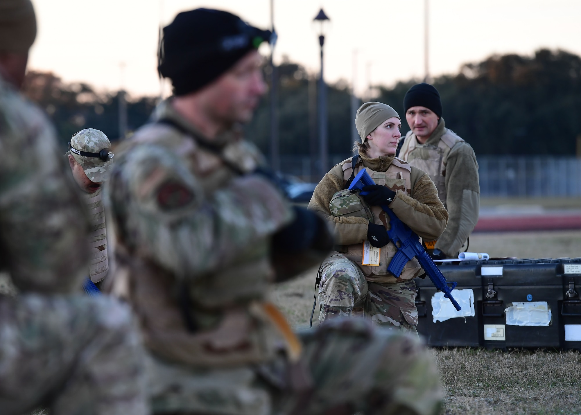 A group of people wearing military uniform take a knee while holding simulated weapons.