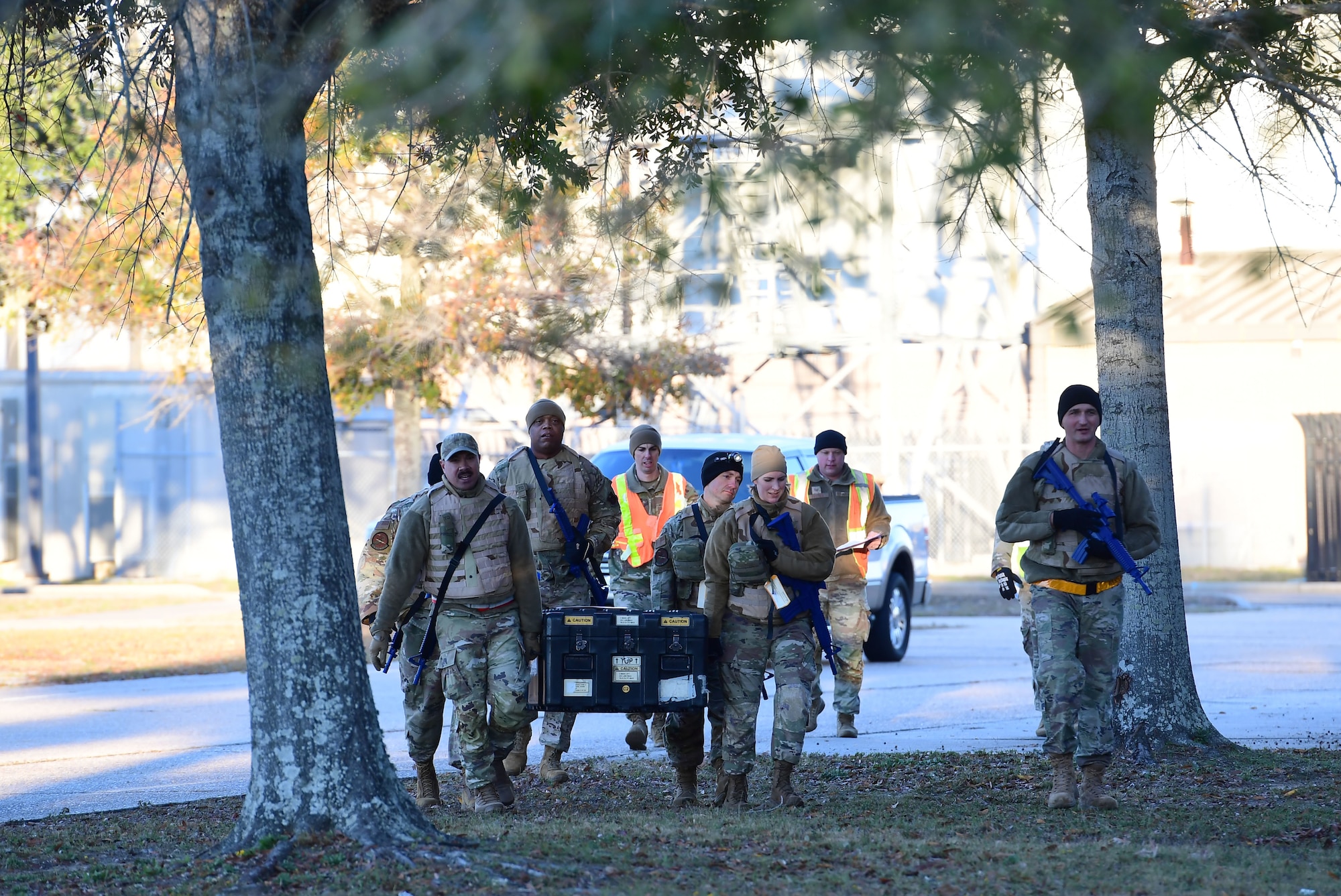 A group of people wearing military uniform carries a large metal box.