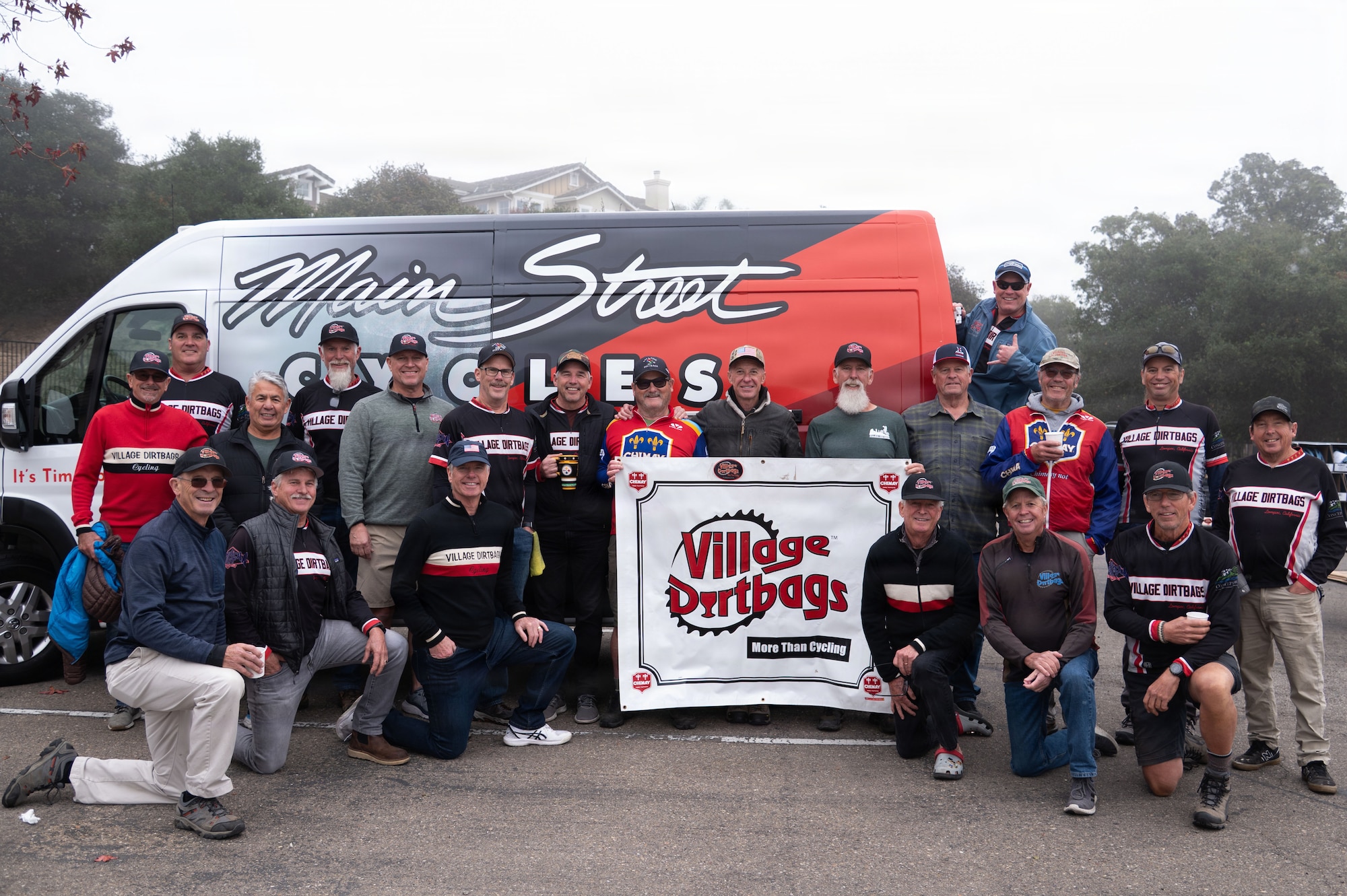 a group of people stand in a parking lot holding a sign reading "village dirtbags"