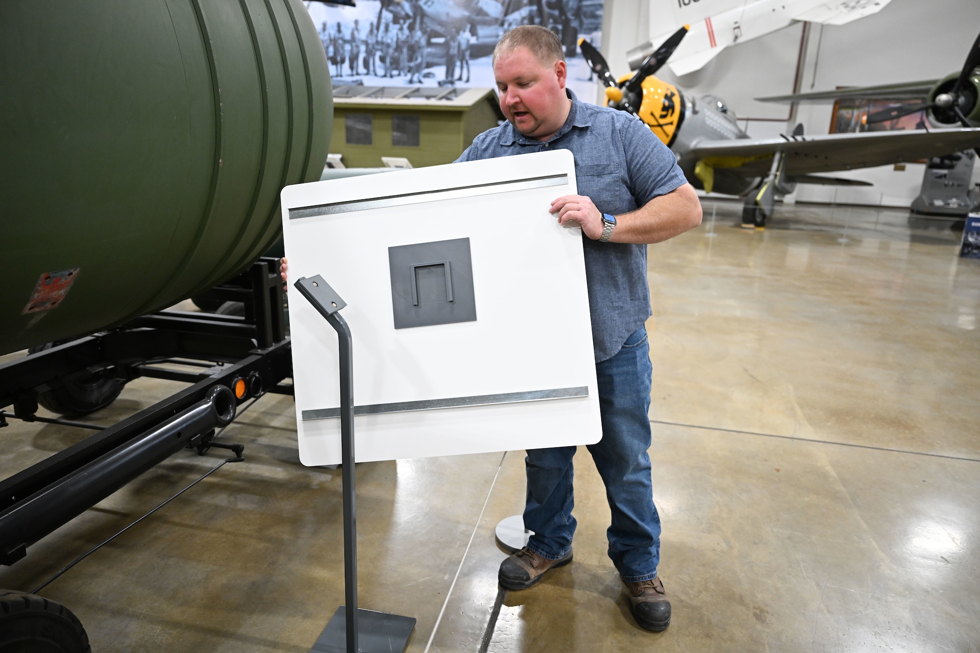 A man holds an aircraft museum exhibit sign to show a 3D printed part holding the sign