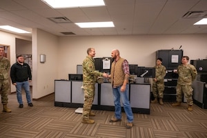 U.S. Air Force Col. Richard Kind, 97th Air Mobility Wing commander, coins Josh Barclay, 97th Operations Support Squadron Radar, Airfield & Weather Systems lead technician, at Altus Air Force Base, Oklahoma, Dec. 15, 2025. Kind presented the 2025 fiscal year Air Education and Training Command (AETC) Airfield Operations Trainer of the Year Award to Barclay to recognize his outstanding performance and reinforce AETC’s commitment to excellence. (U.S. Air Force photo by Airman 1st Class Emma Wright)