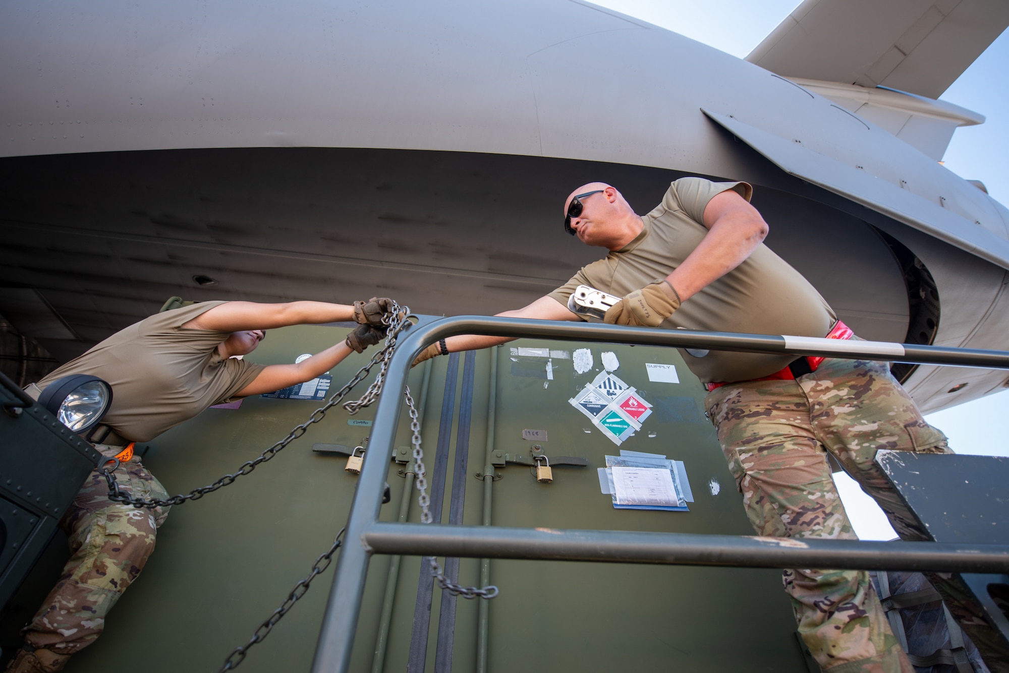 Senior Airman Savana Gallagher, left, an aerial porter from 735th Air Mobility Squadron, hands chains to secure cargo to Master Sgt. Jerome Noltemeyer, an aerial porter from the 123rd Logistics Readiness Squadron, at Joint Base Pearl Harbor-Hickam, Hawaii, on Aug. 5, 2025. Noltemeyer was among more than 75 personnel from the Louisville-based 123rd Airlift Wing to conduct annual training here over 15 days, sharpening skills that enhance their employment as Multi-Capable Airmen. (U.S. Air National Guard photo by Phil Speck)
