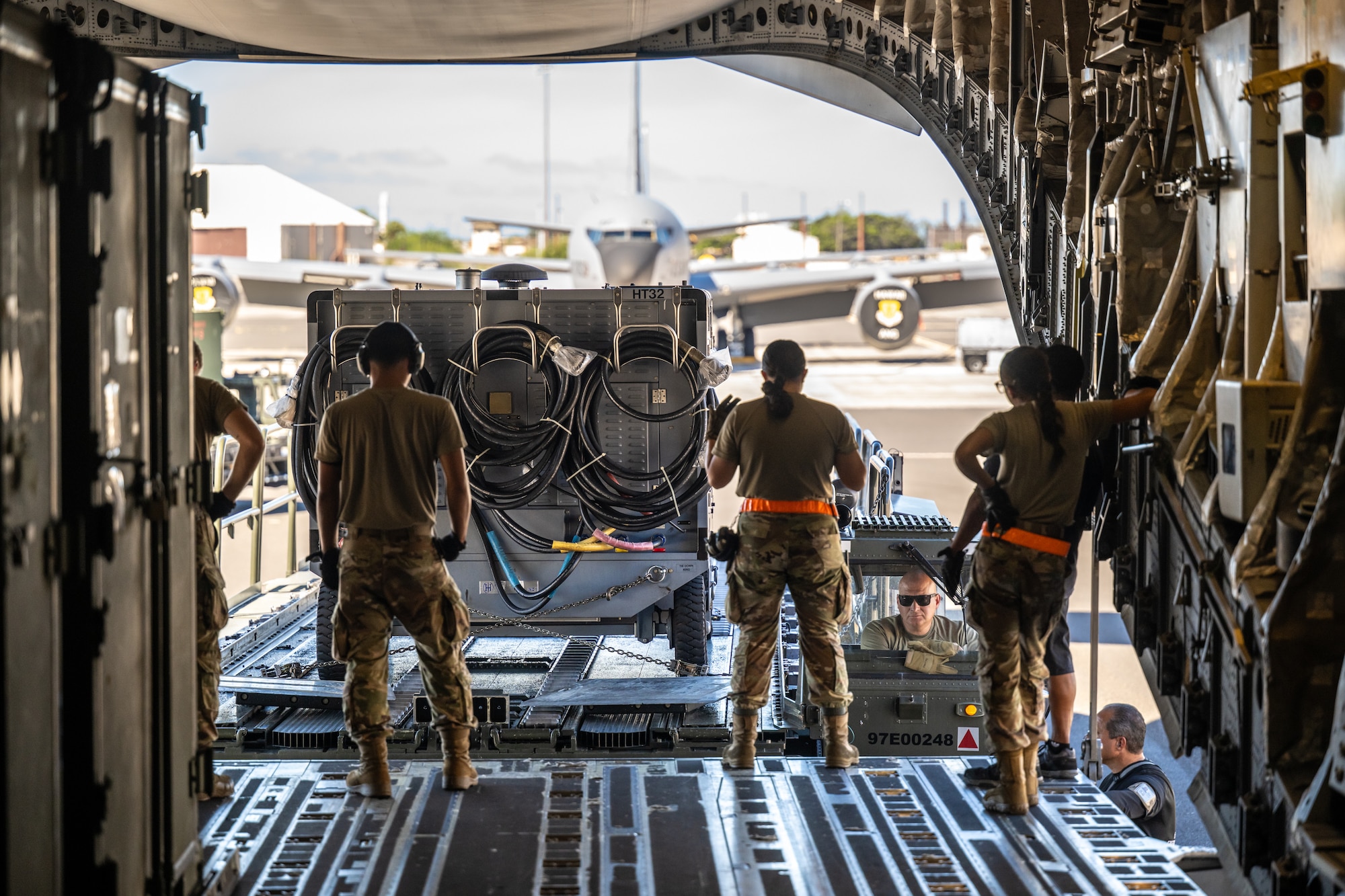 An Airman from the 735th Air Mobility Squadron directs Master Sgt. Jerome Noltemeyer of the Kentucky Air National Guard’s 123rd Logistics Readiness Squadron Nolte as he positions a Tunner cargo loader behind a U.S. Air Force C-17 Globemaster II aircraft at Joint Base Pearl Harbor-Hickam, Hawaii, on Aug. 5, 2025. Noltemeyer was among more than 70 personnel from the Louisville-based 123rd Airlift Wing to conduct annual training here over 14 days, sharpening skills that enhance their global employment as Multi-Capable Airmen. (U.S. Air National Guard photo by Dale Greer)