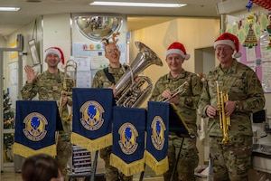 Airmen hold musical instruments, smiling as they greet patients in a hospital.