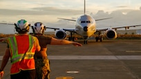 An Aviation Structural Mechanic directs a U.S. Navy P-8A Poseidon aircraft on a flight line.