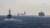 A multinational naval strike group, including U.S. Navy destroyers and an aircraft carrier, sails in formation.